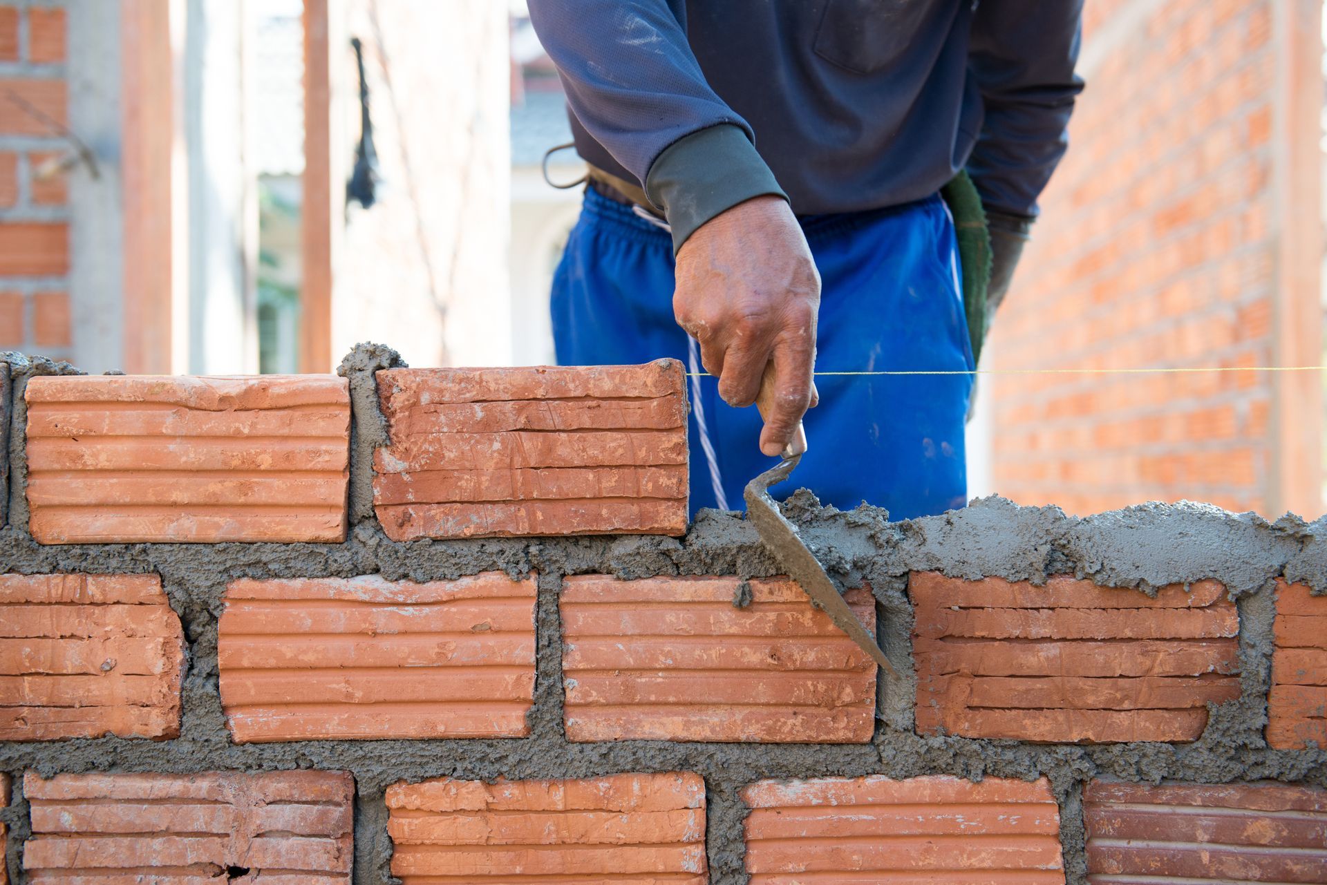 Bricklayer troweling wet mortar on a red brick wall under construction