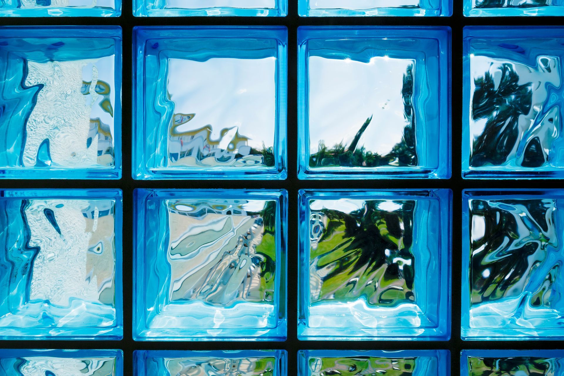 Blue glass block window with abstract reflections of sky and trees