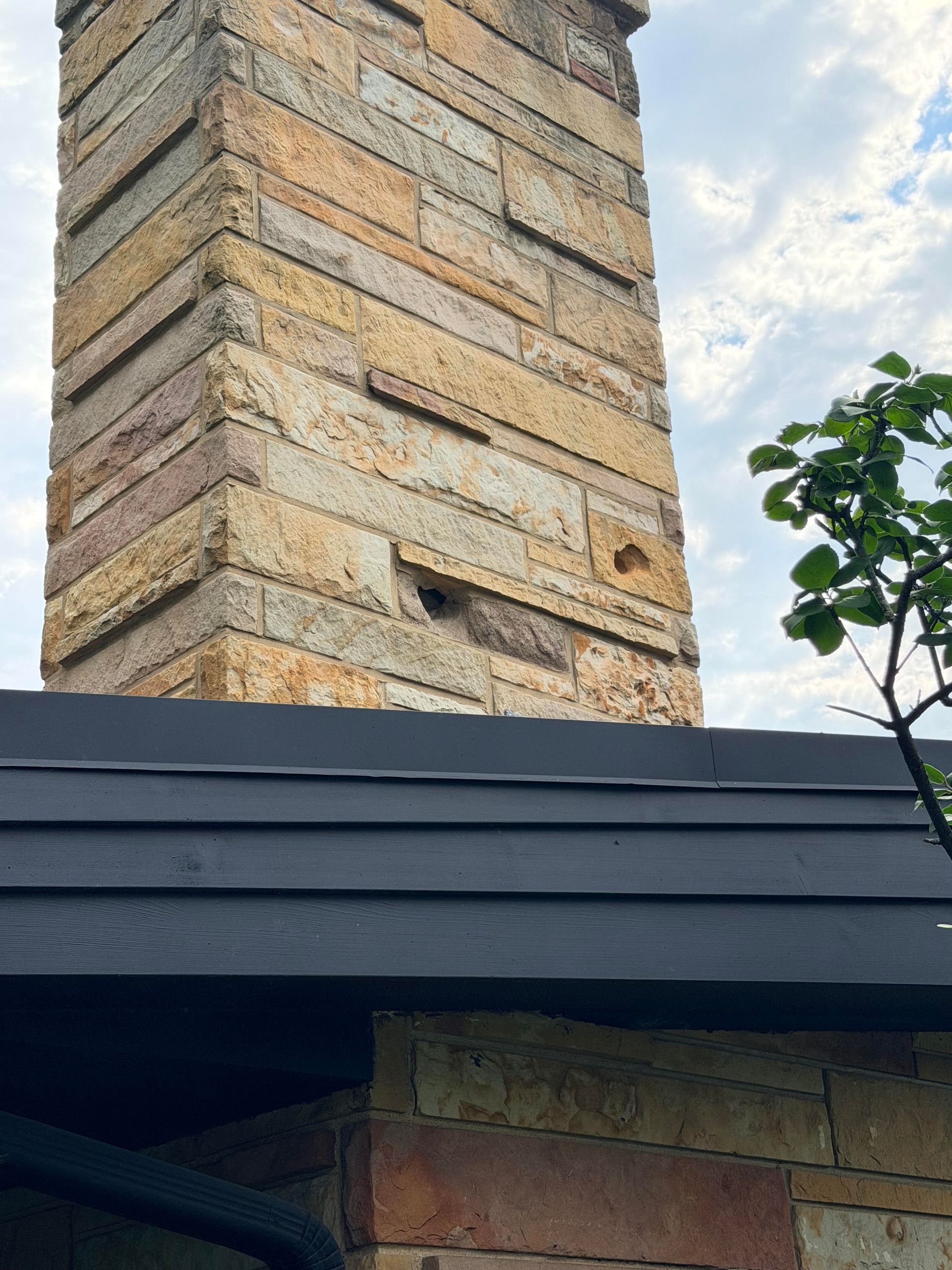 Brick chimney on a gray-shingled house roof against a blue sky
