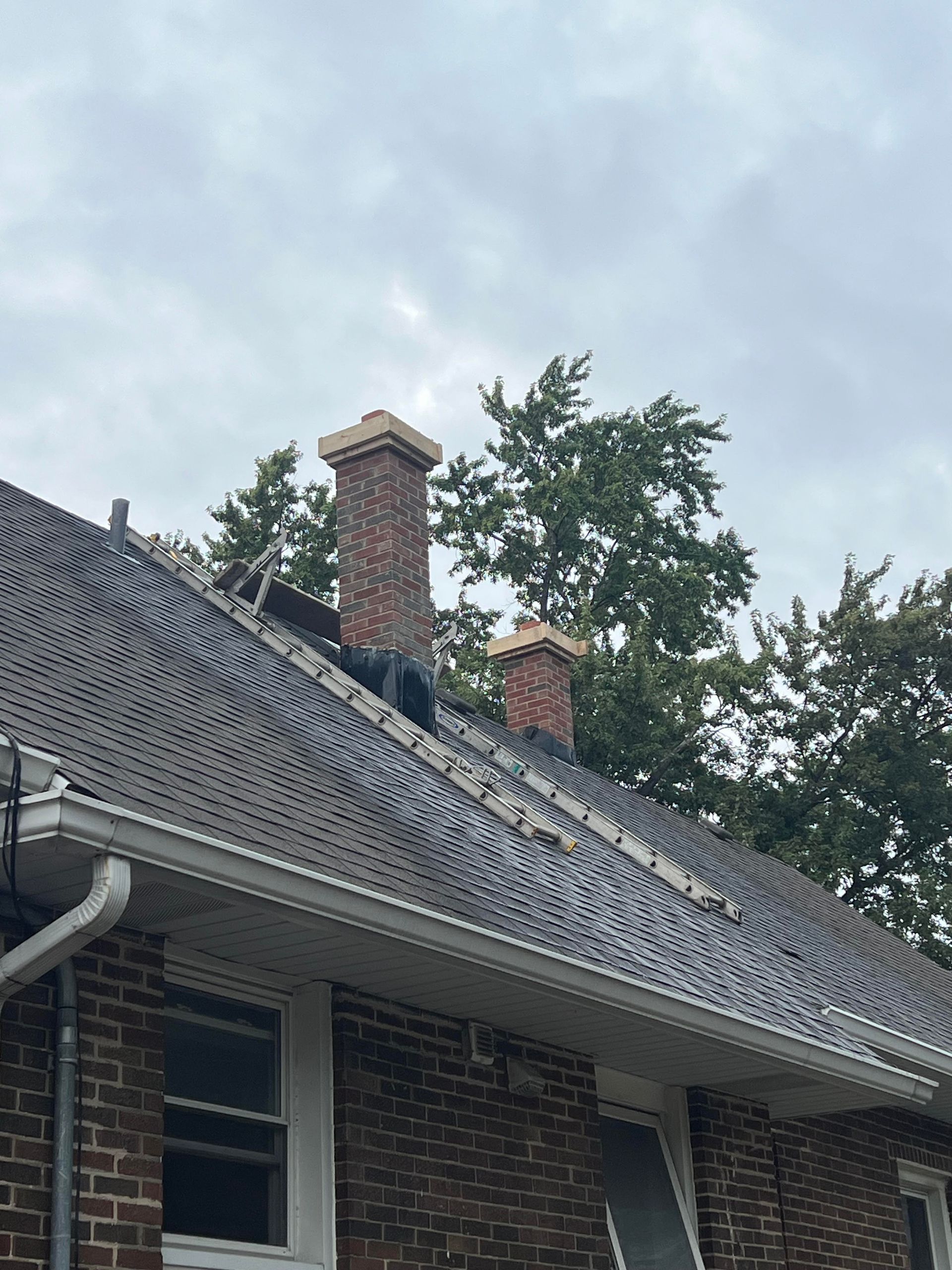 Orange brick chimney with black cap on a shingled roof against a pale sky
