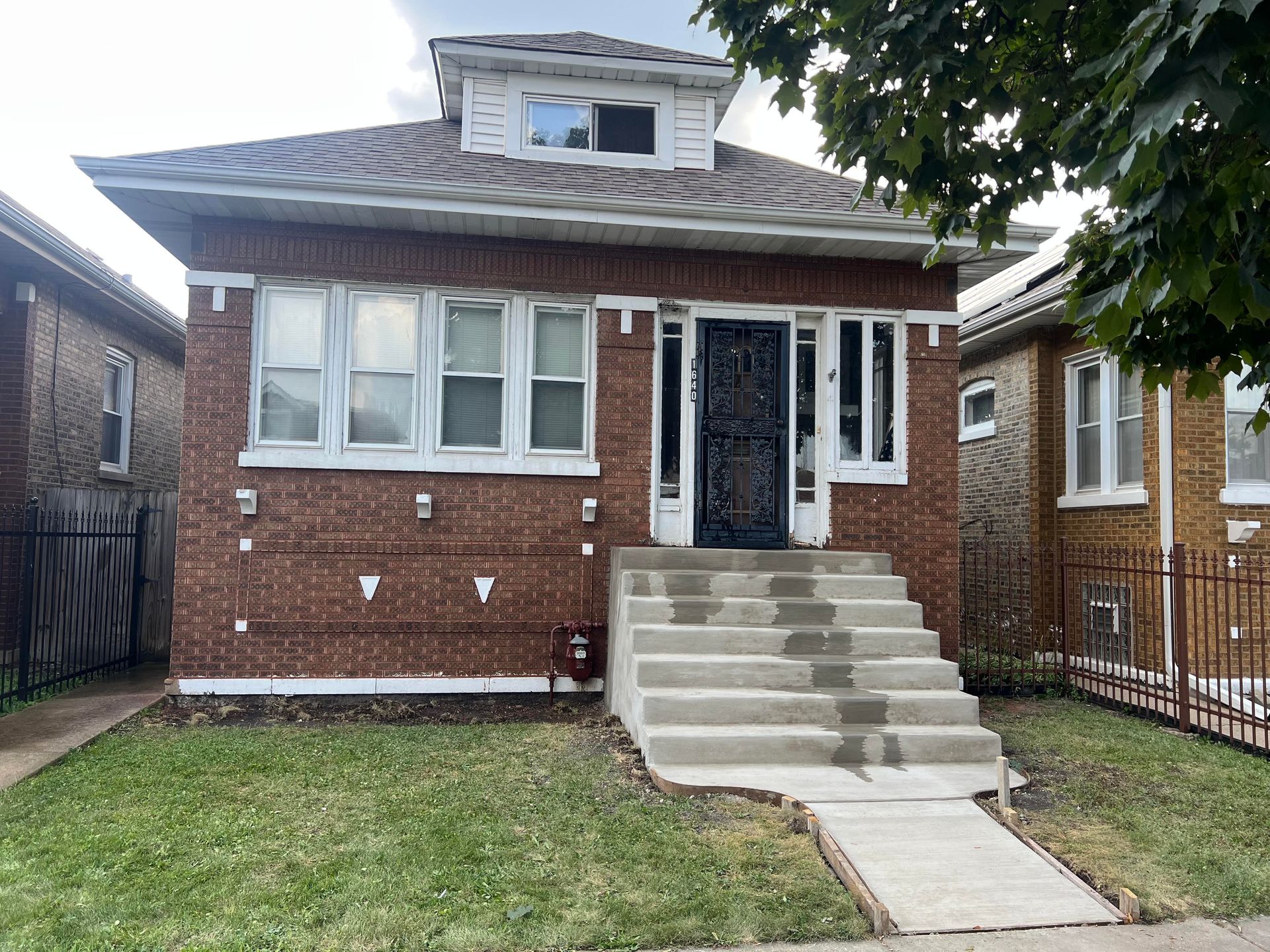 Brick suburban house with black shutters, white trim, and a green lawn under a partly cloudy sky