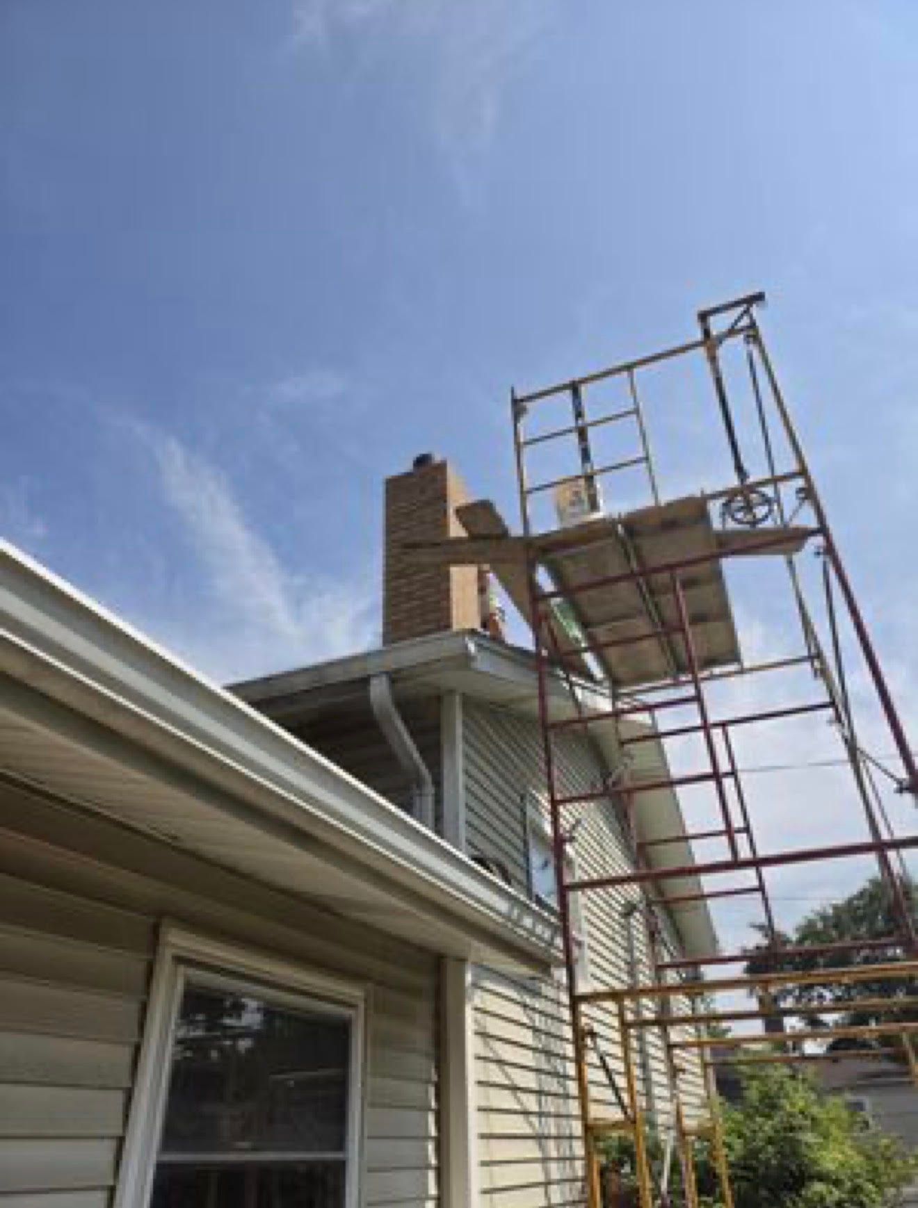 Brick chimney above a dark shingled roof against a blurred outdoor background