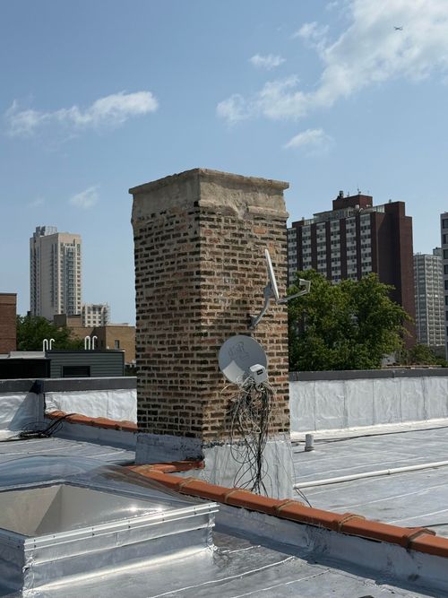 White house roof with red brick chimney against a clear blue sky