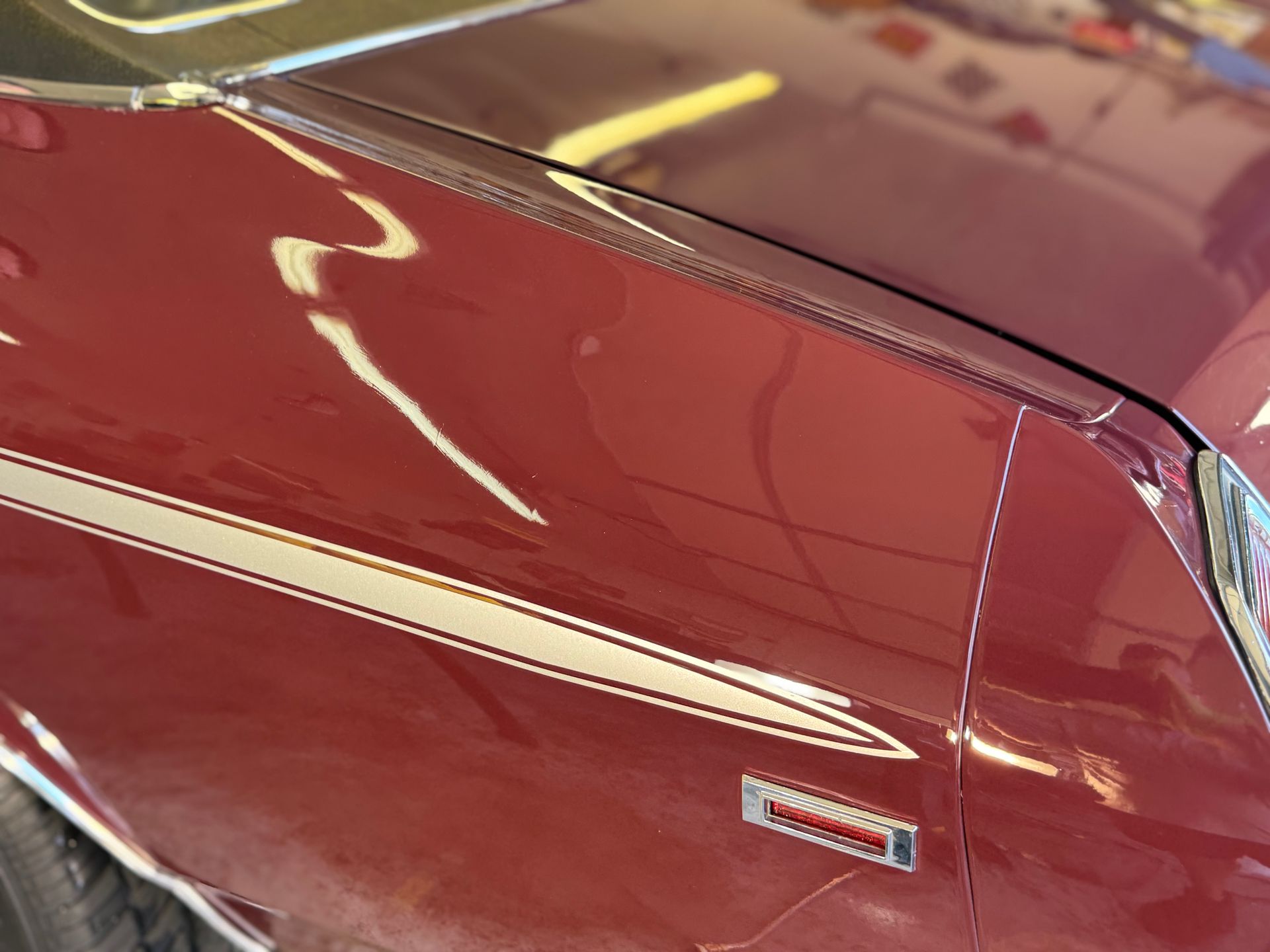 Maroon car fender with silver stripe and chrome emblem.