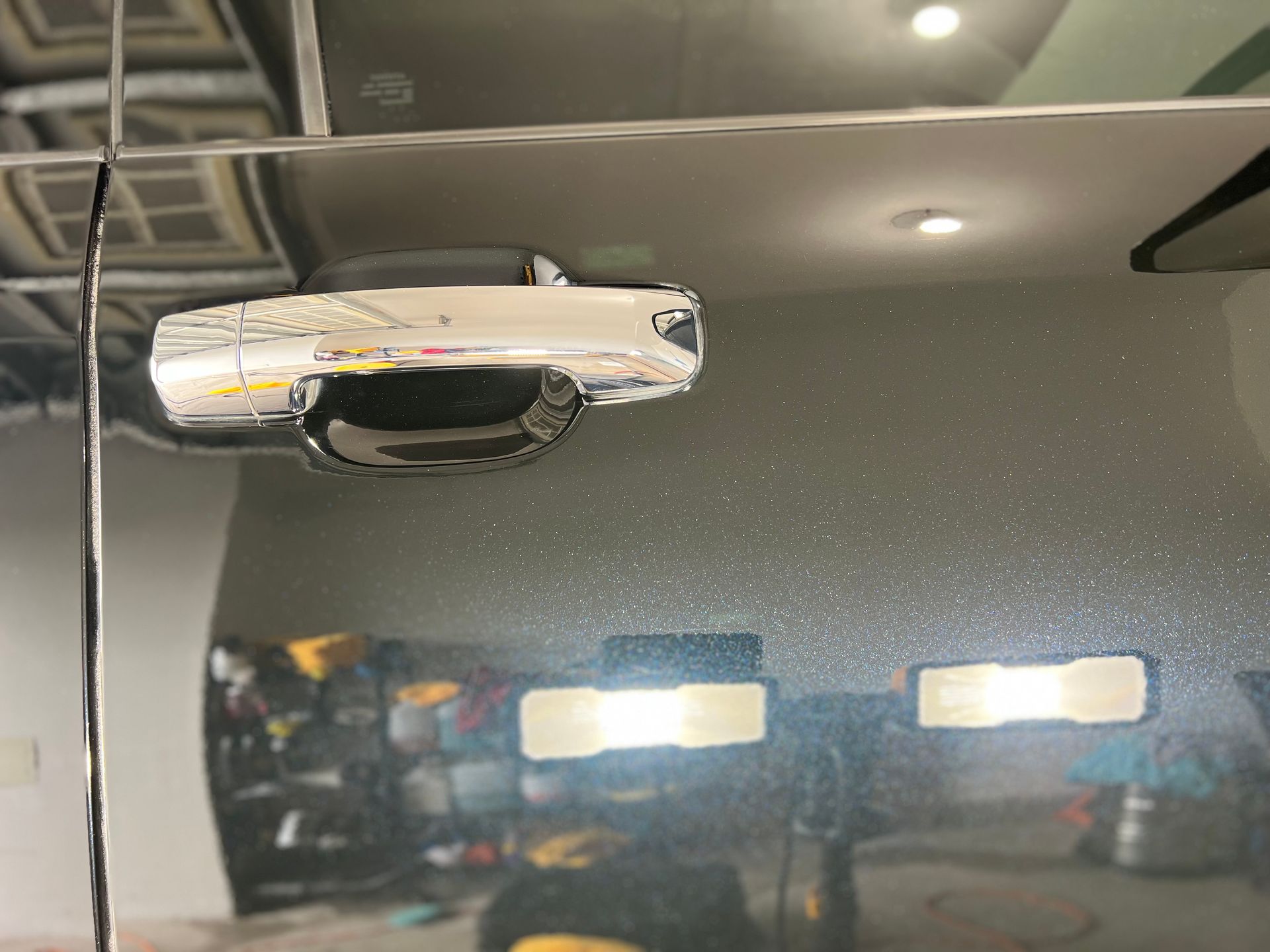 Chrome car door handle on a reflective, dark-colored car door. Garage setting.