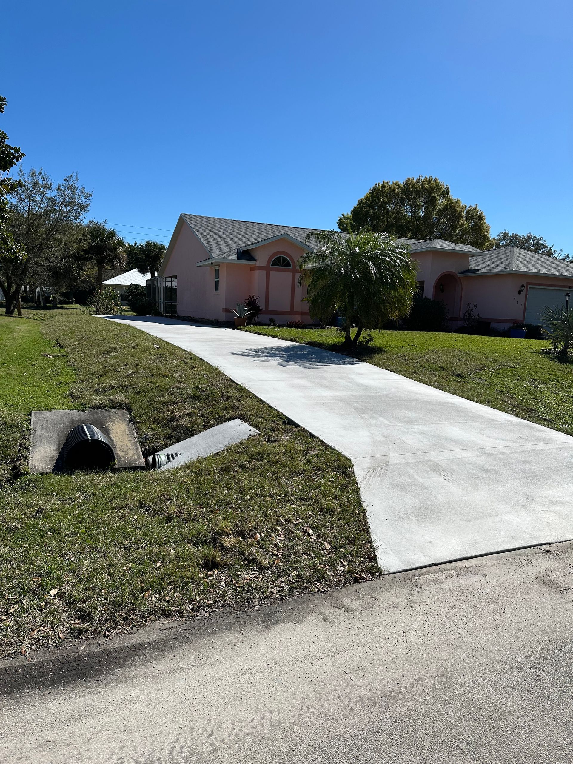 Suburban house with pink exterior and a white driveway on a sunny day