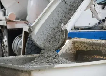 Wet concrete pouring from a chute into a wheelbarrow at a construction site