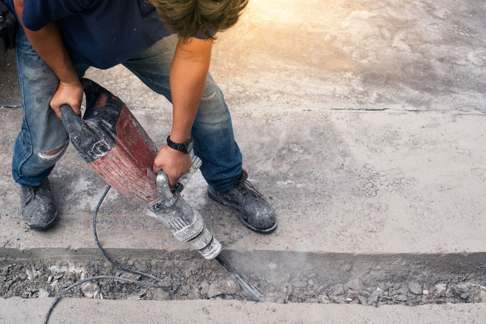 Worker using a jackhammer to break concrete along a pavement edge