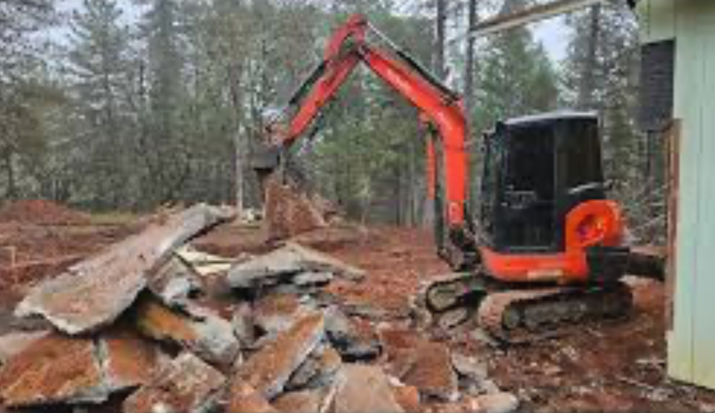 Red excavator clearing rubble in a muddy wooded construction site
