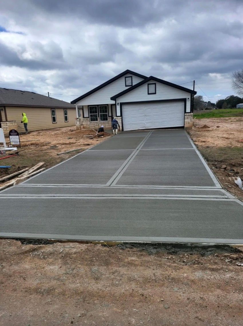 Fresh concrete driveway leading to a white house with a two-car garage under a cloudy sky