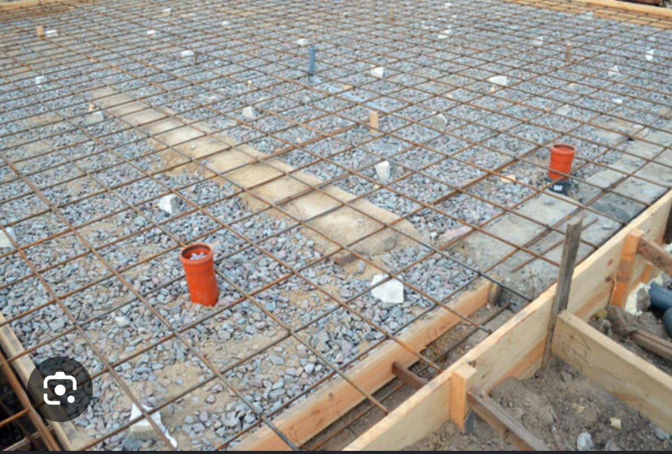 Rebar grid for a concrete slab with red pipe stubs and wooden formwork at the edge