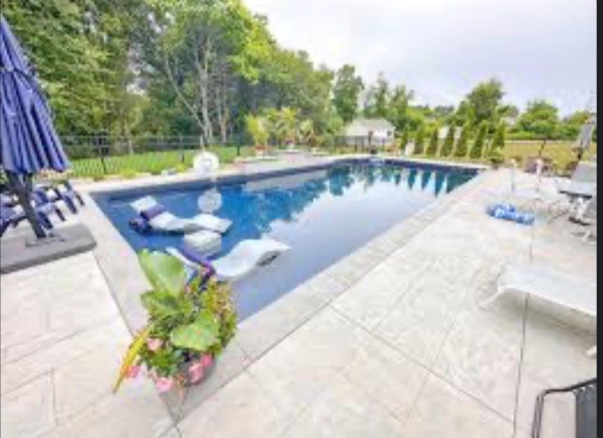 Backyard pool with blue water, lounge chairs, and patio seating surrounded by greenery