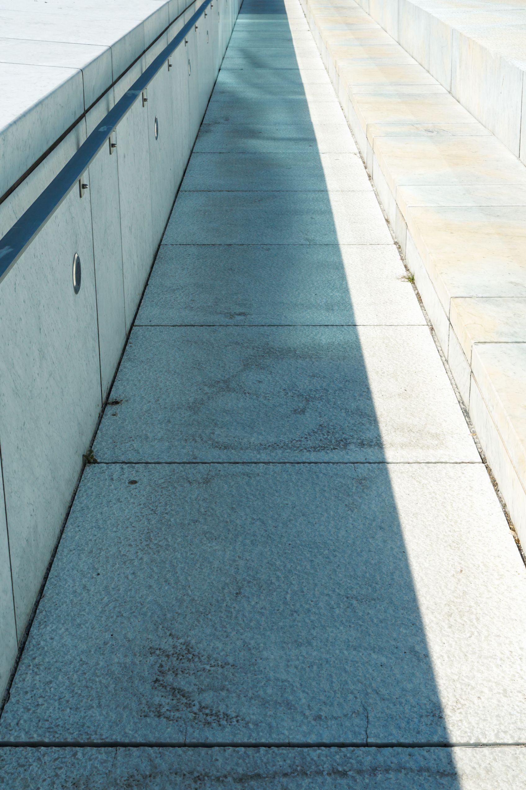 Empty concrete walkway with long shadows between pale walls outdoors