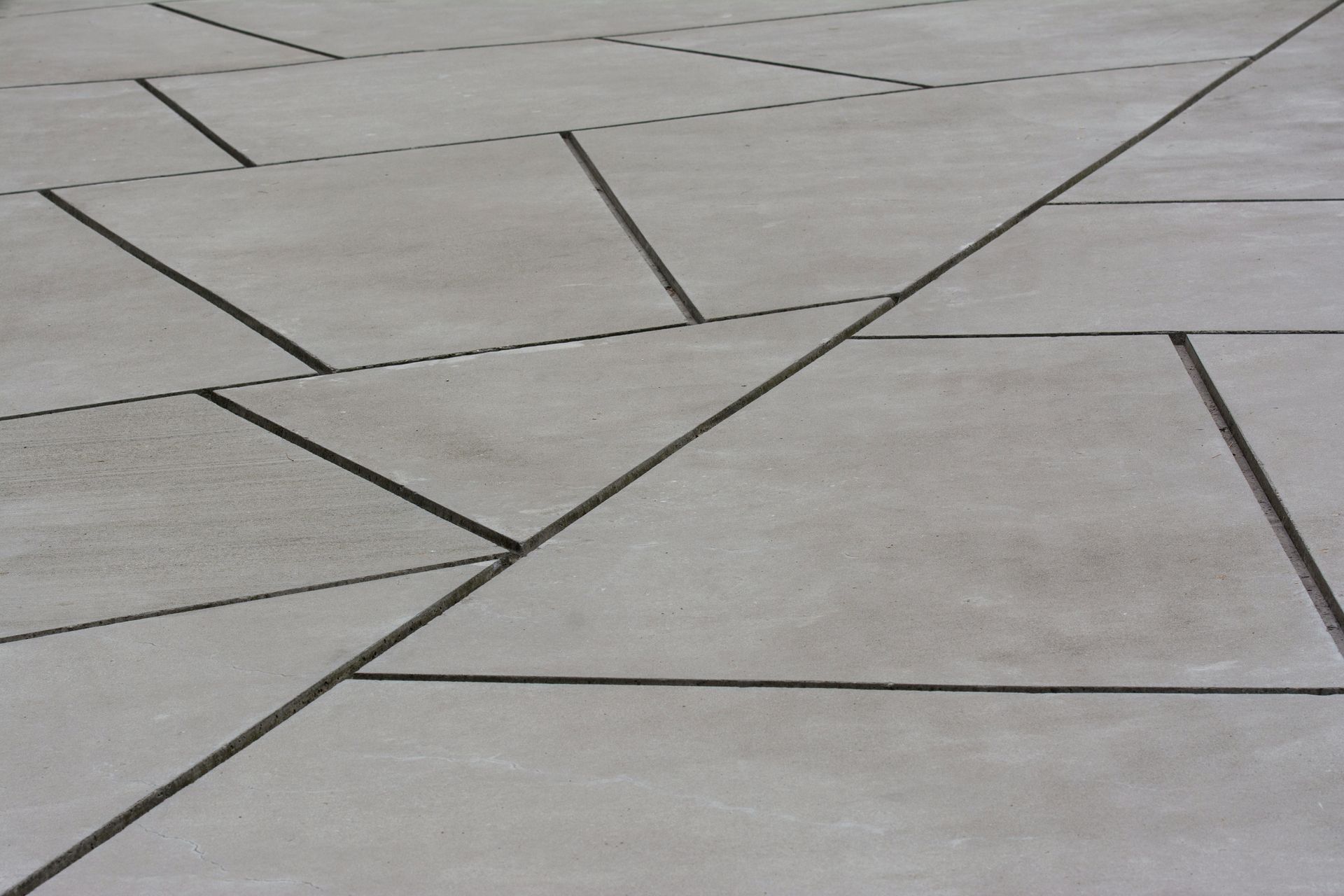 Gray concrete pavement with angular slab seams and dark grout lines forming geometric patterns