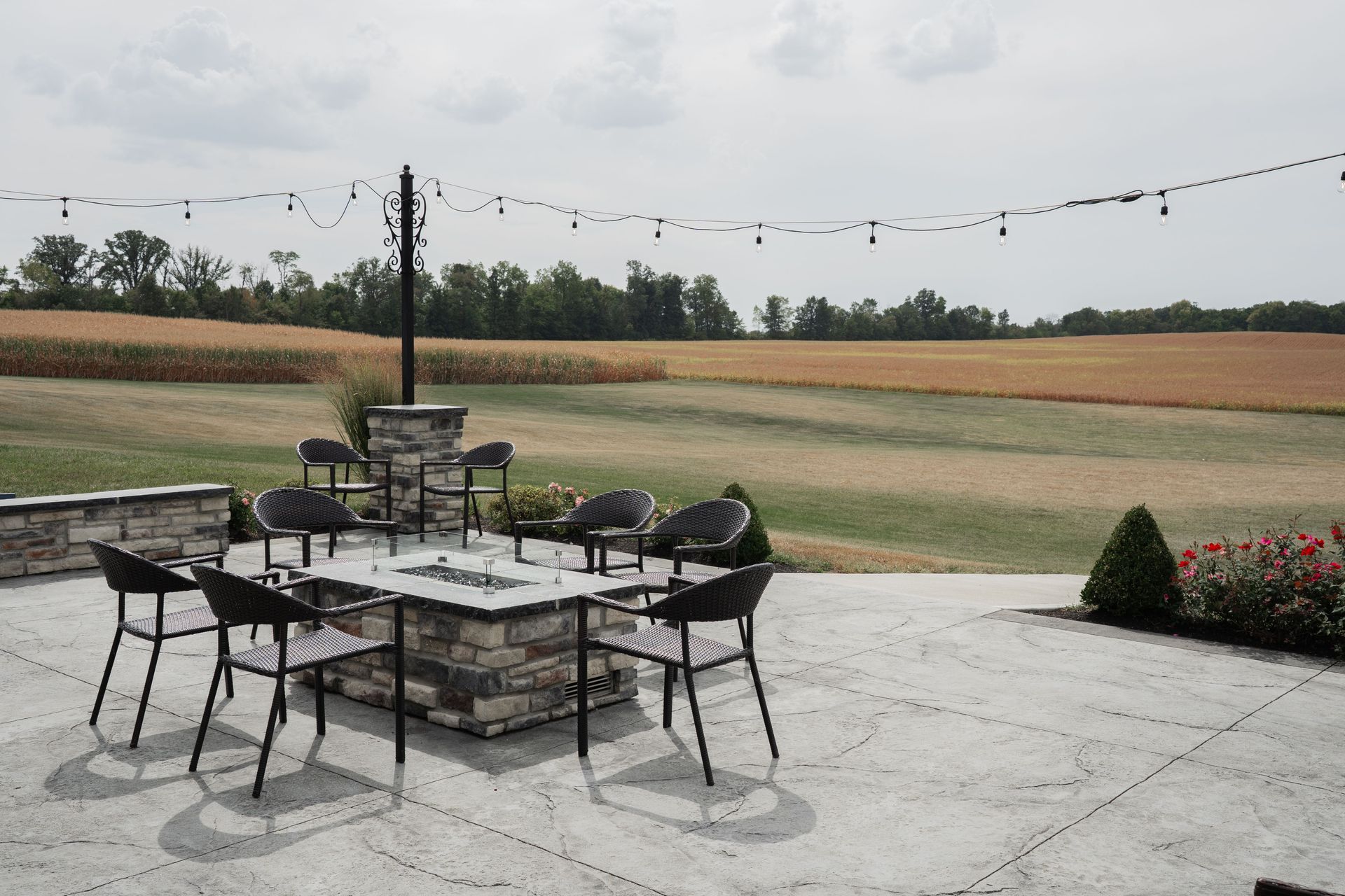 Patio dining set on a stone terrace overlooking open fields under a cloudy sky
