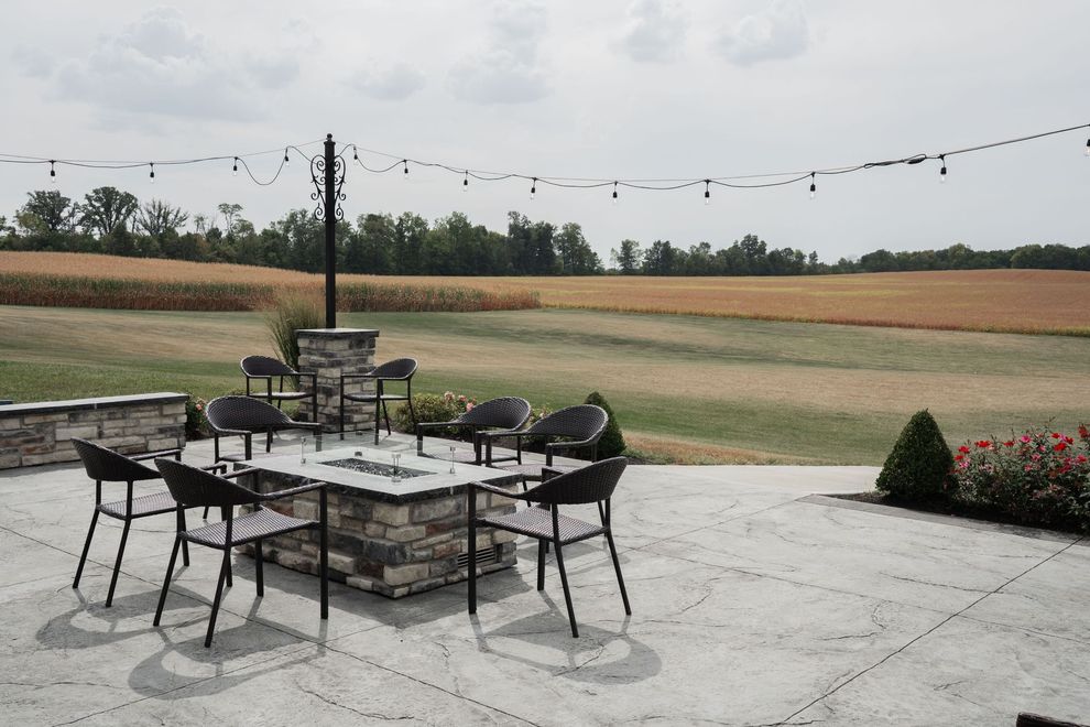 Patio dining set on a stone terrace overlooking open fields under a cloudy sky