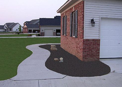 Curved concrete walkway along a brick house, bordered by black mulch and a green lawn.