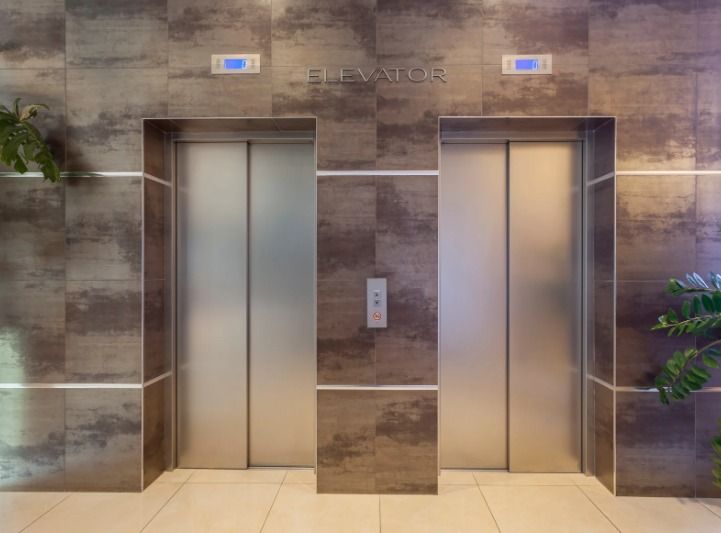 Two stainless steel elevator doors in a stone-walled lobby with a call button panel between them