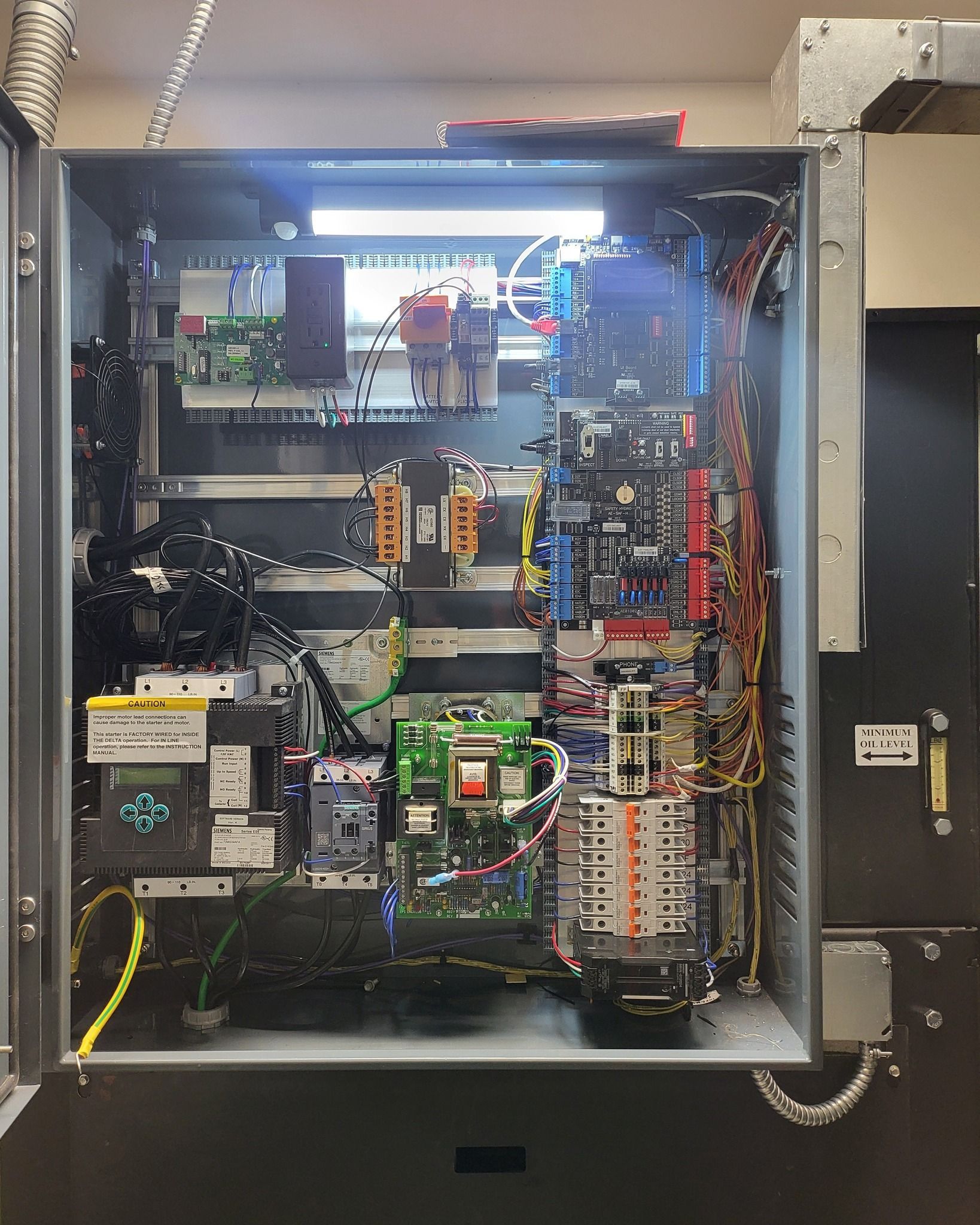 Open electrical control panel with wiring, circuit boards, relays, and terminal blocks mounted inside.