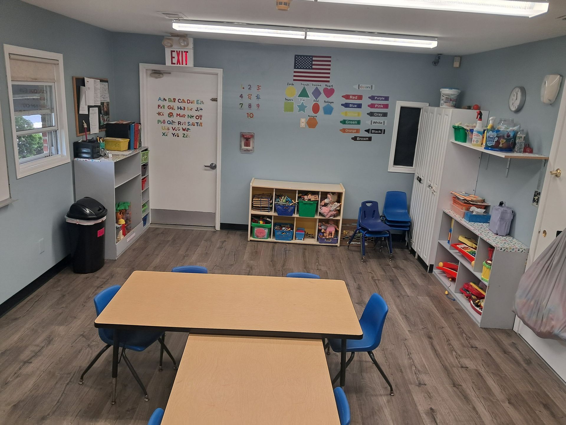 Small classroom with tables, blue chairs, shelves, wall decorations, and a whiteboard.