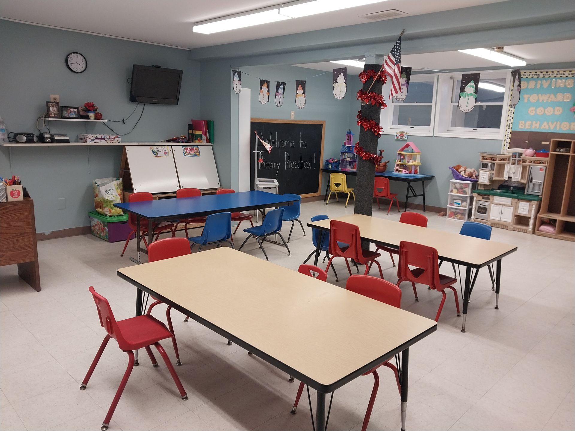 Childcare classroom with cribs, play areas, blue table, and hanging decorations