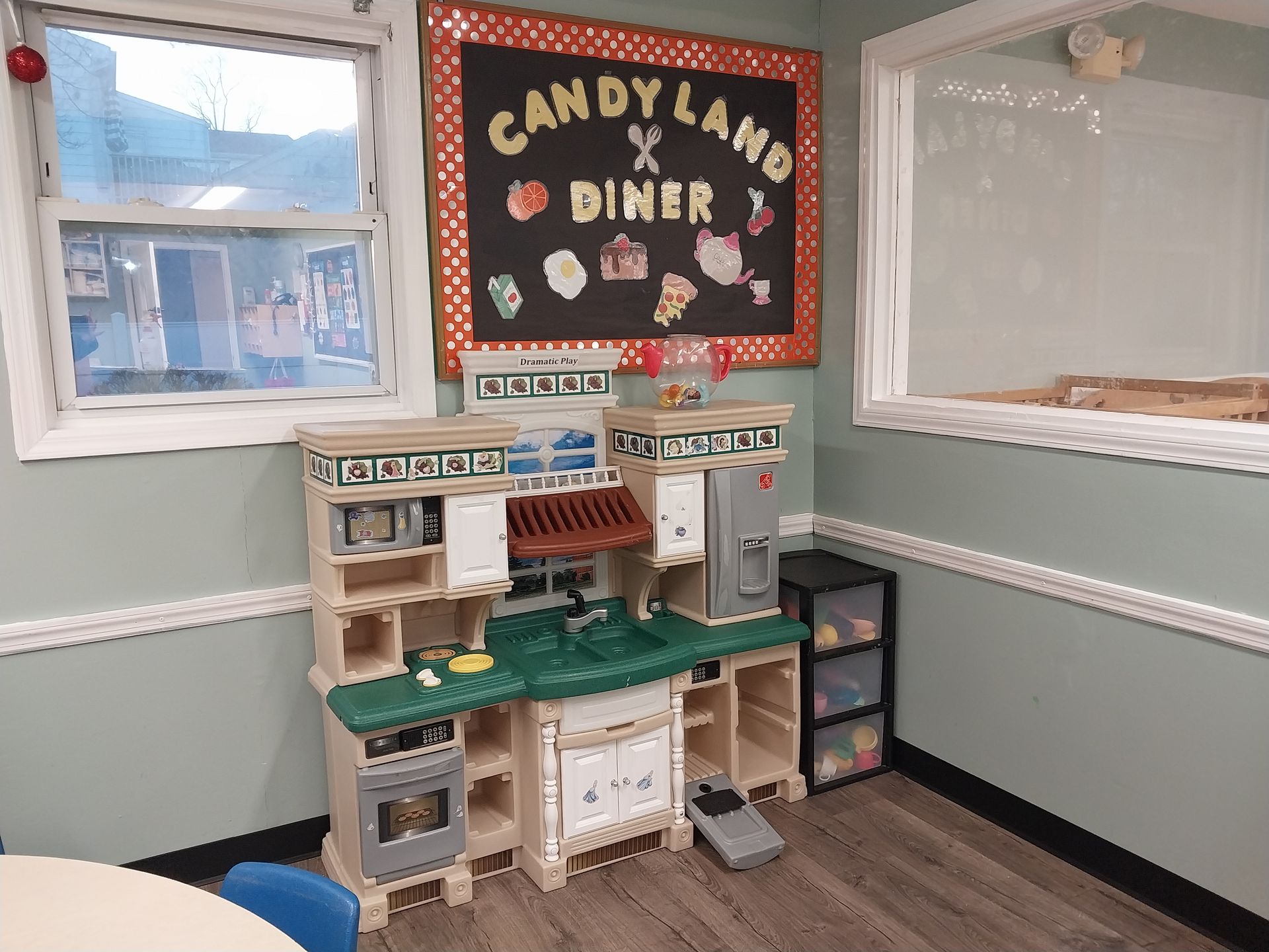 Small play diner with toy kitchen set beneath a “Candyland Diner” sign in a light blue room