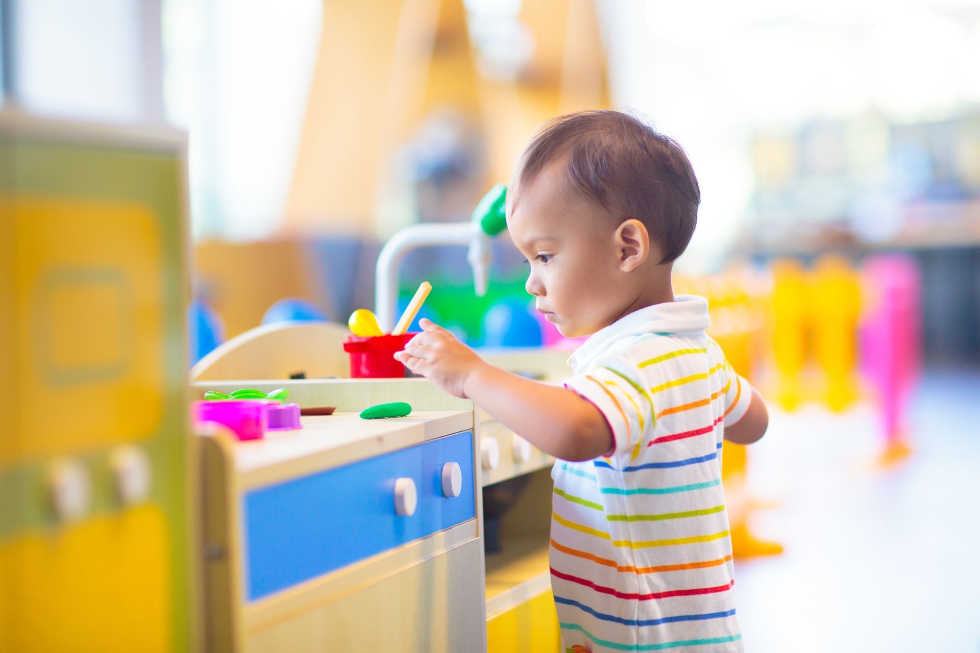 Child playing with colorful toys at a play table in a bright indoor classroom.