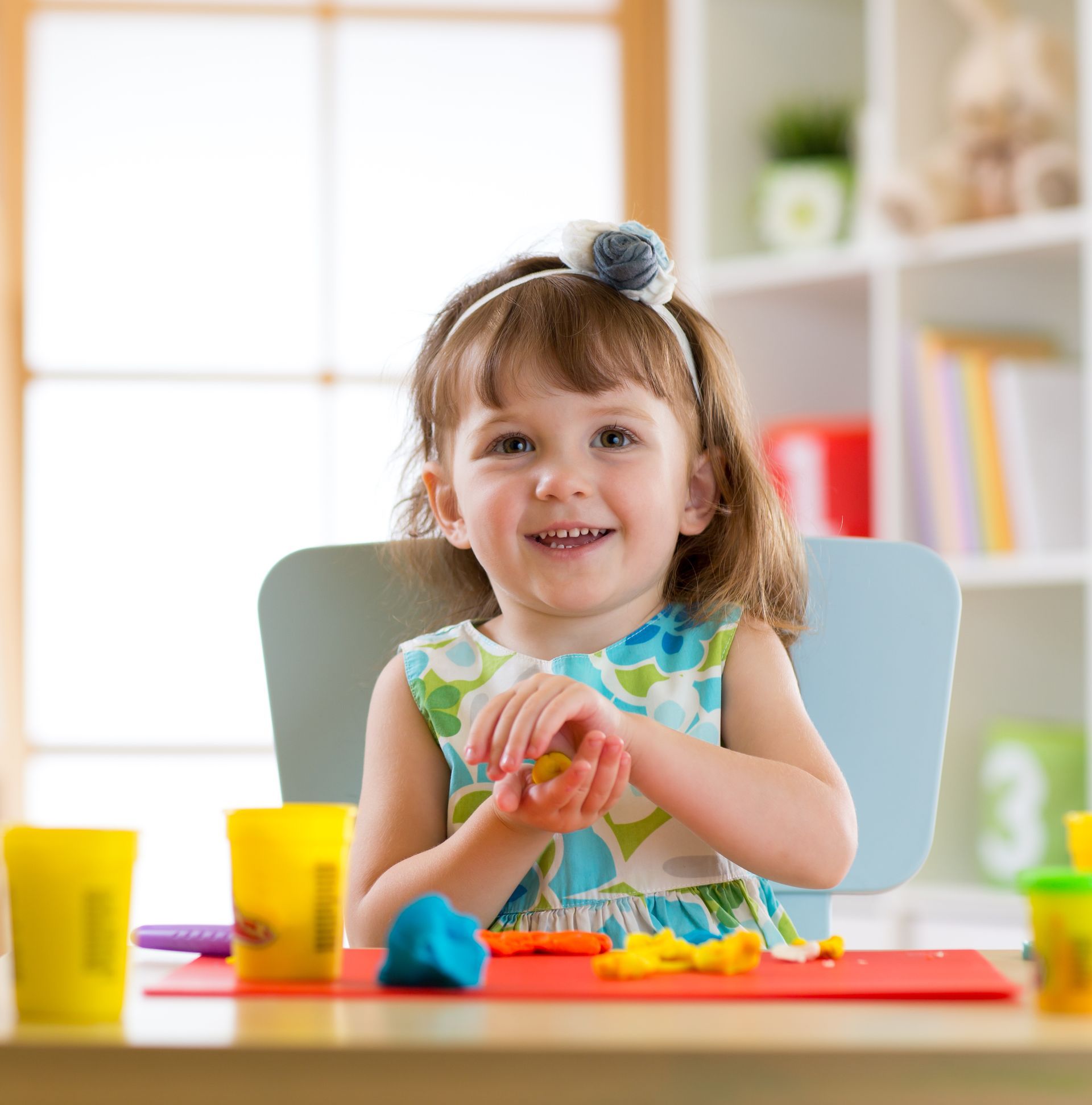 Smiling child molding colorful clay at a table in a bright playroom