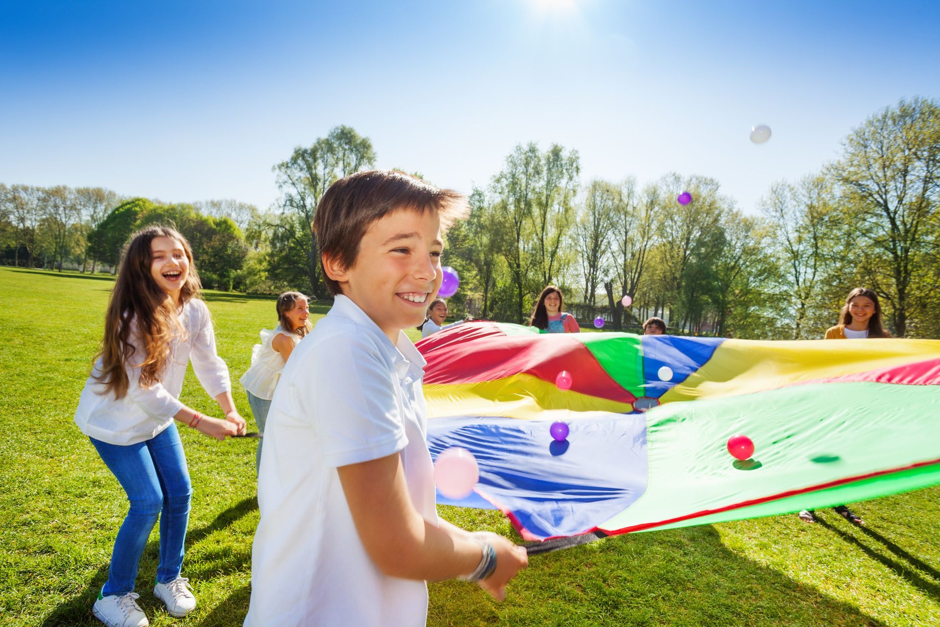Children playing with a colorful parachute on a sunny grassy field