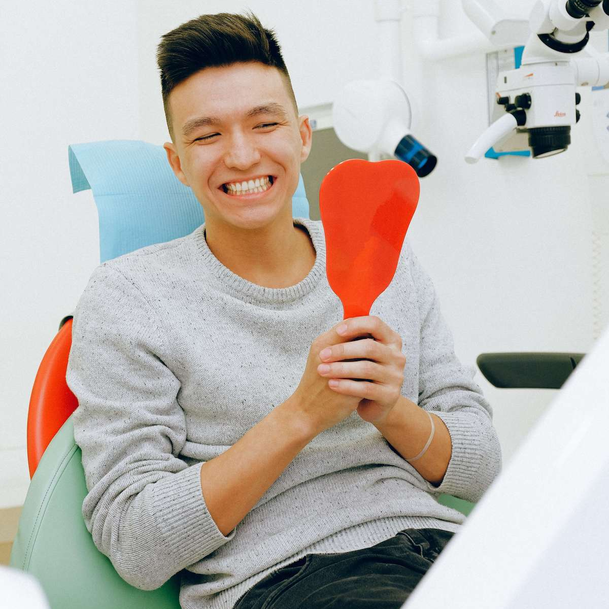 A man is sitting in a dental chair holding a red heart shaped mirror
