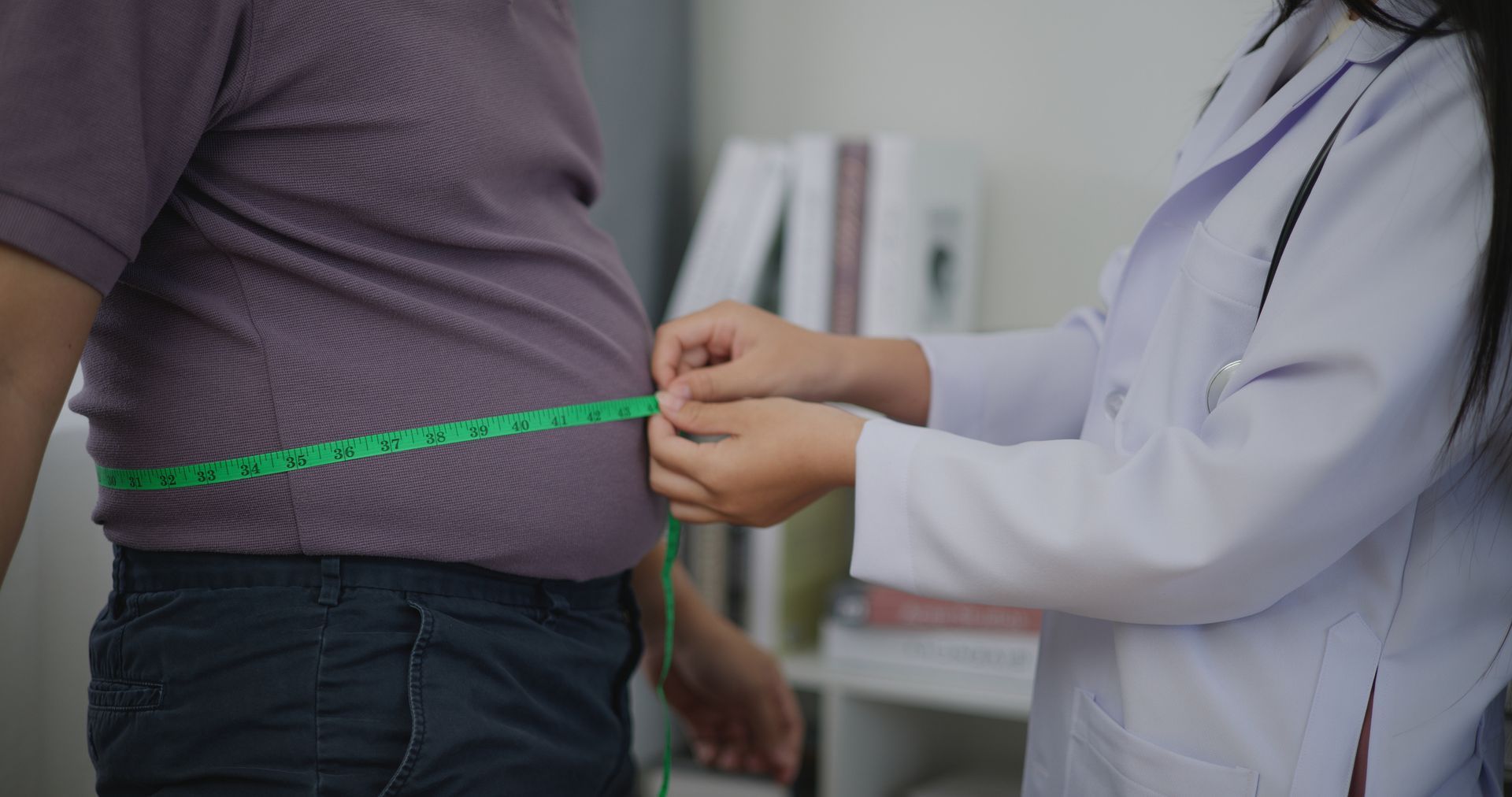 A doctor is measuring a man 's waist with a tape measure.