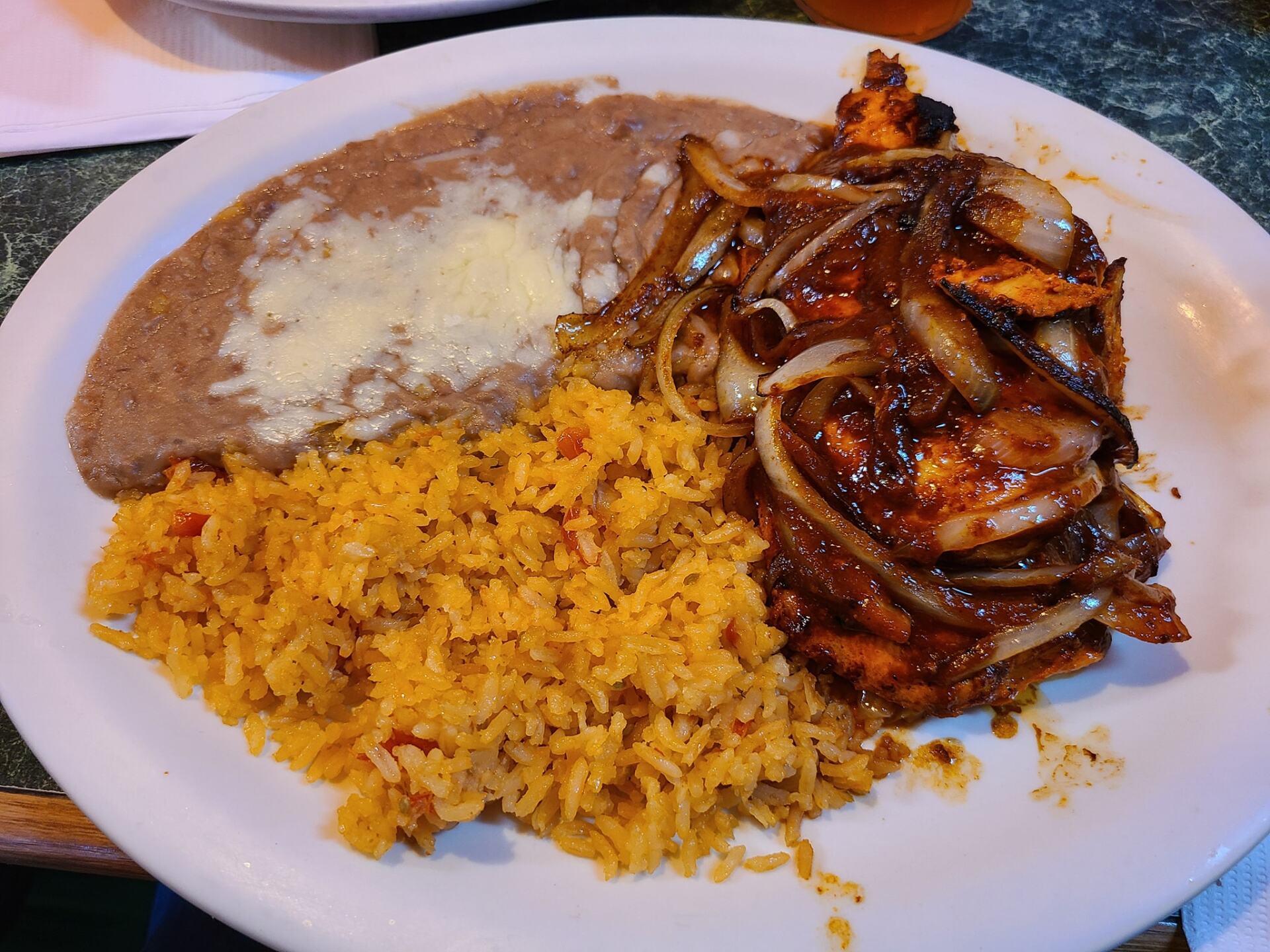 Plate with Mexican food: refried beans, rice, and chicken with onions.