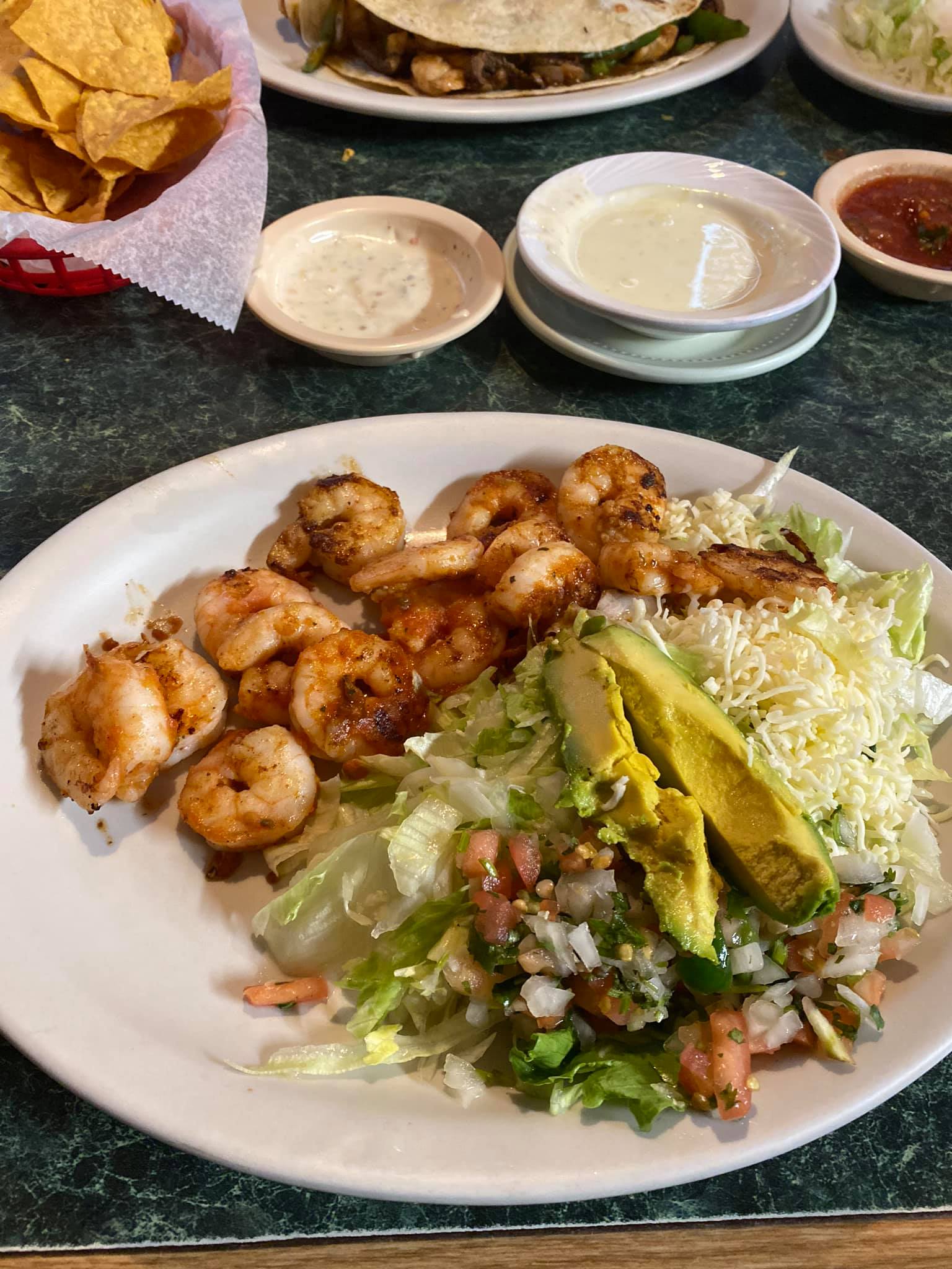 Plate of grilled shrimp, salad with avocado, and small side dishes.