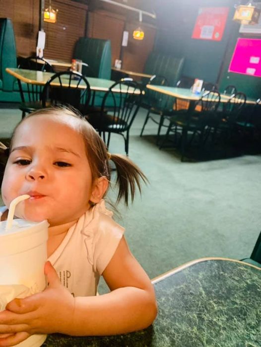 Young child drinking from a white cup with a straw in a diner booth.