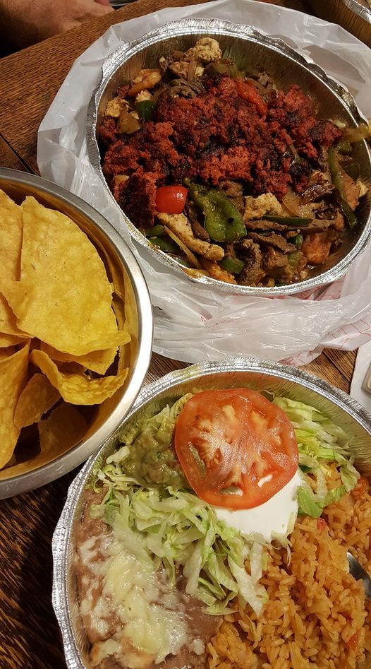 Mexican food spread: chips, beans with toppings, and a dish with red meat and vegetables.