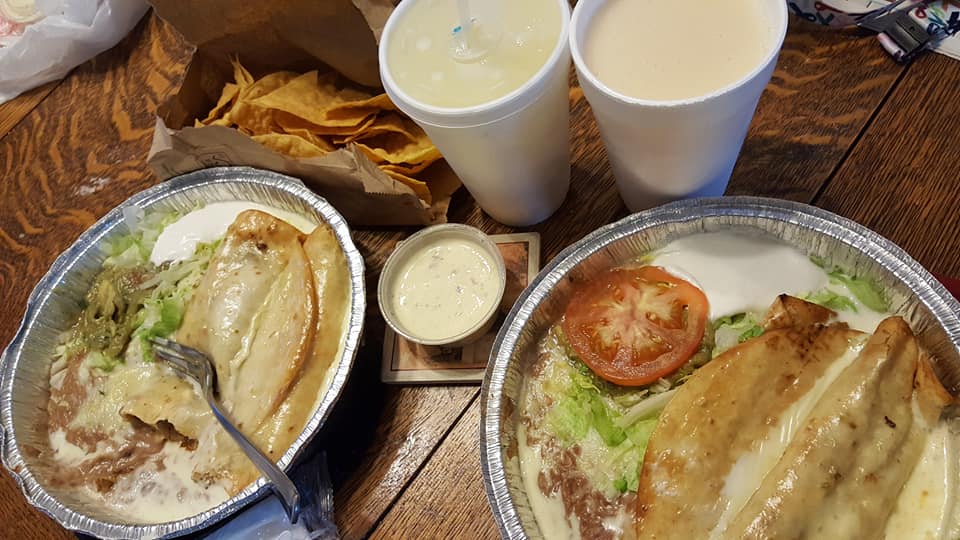 Two chicken meals, drinks, and chips on a wooden table.