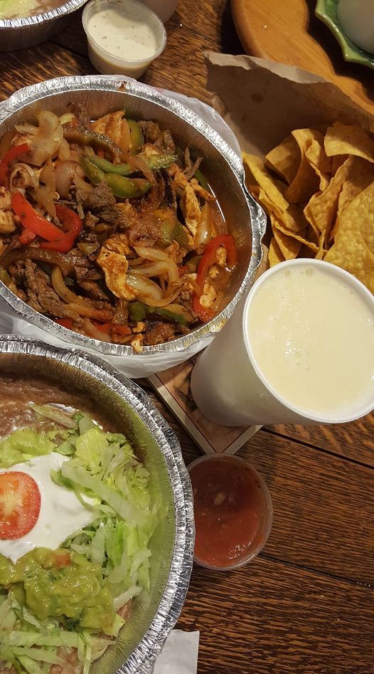 Fajitas with vegetables, chips, salsa, a margarita, and a topped dish on a wooden table.