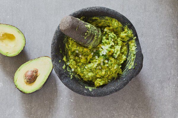 Avocado halves next to a mortar and pestle with guacamole.