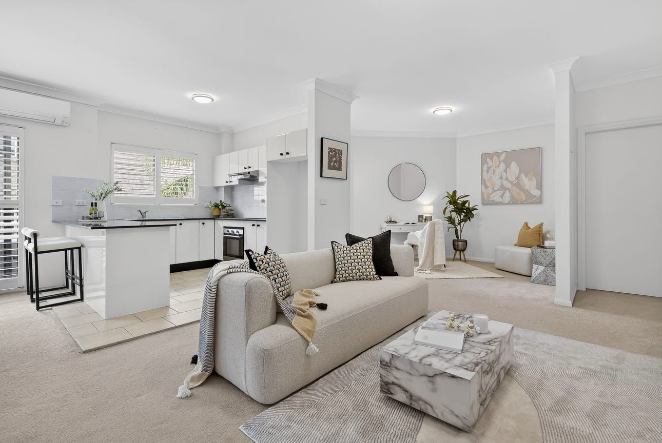 A Bright Open-plan Living Room With a Beige Sofa, Patterned Ottoman, and a Kitchen — Brightside Buyers Agency in Dundas, NSW