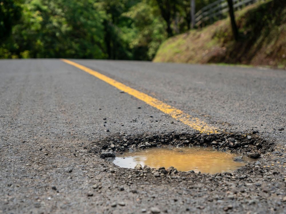 A pothole on the side of a road with a puddle of water in it.