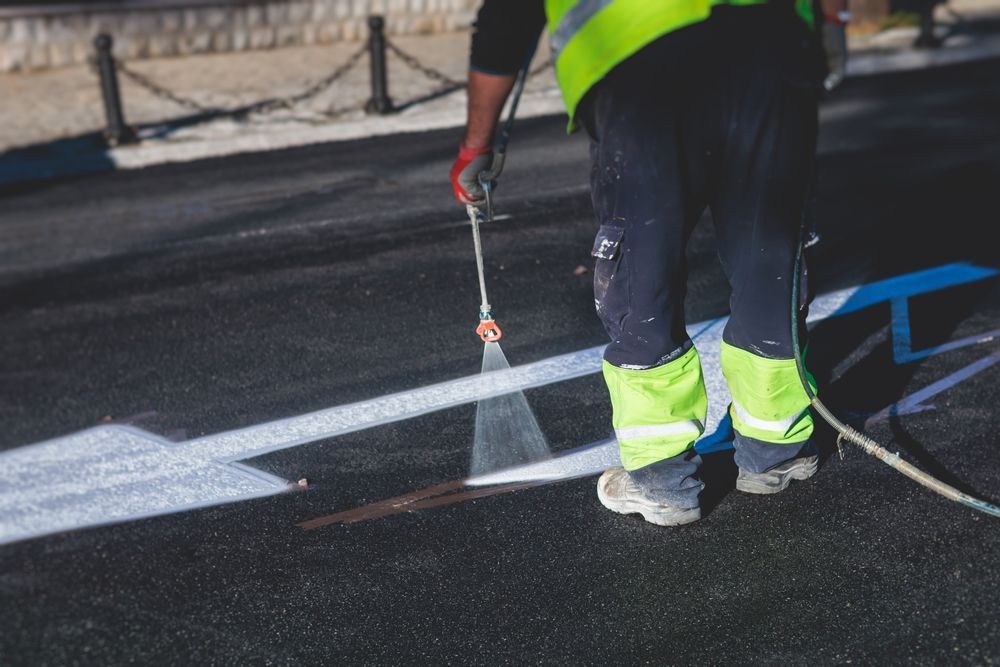 A man is spraying paint on the road with a sprayer.