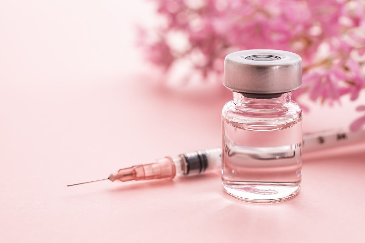 A bottle of liquid and a syringe on a pink background.