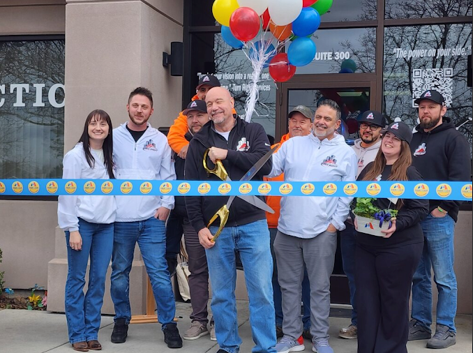 People standing at a ribbon-cutting ceremony with colorful balloons outside a building