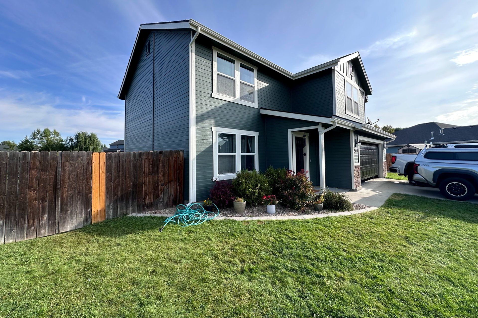 Two-story blue house with a front porch, fenced yard, and parked truck in daylight.