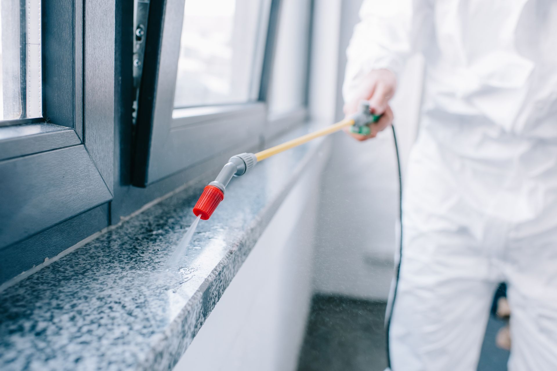 Person spraying a window sill with a handheld sprayer during interior cleaning.
