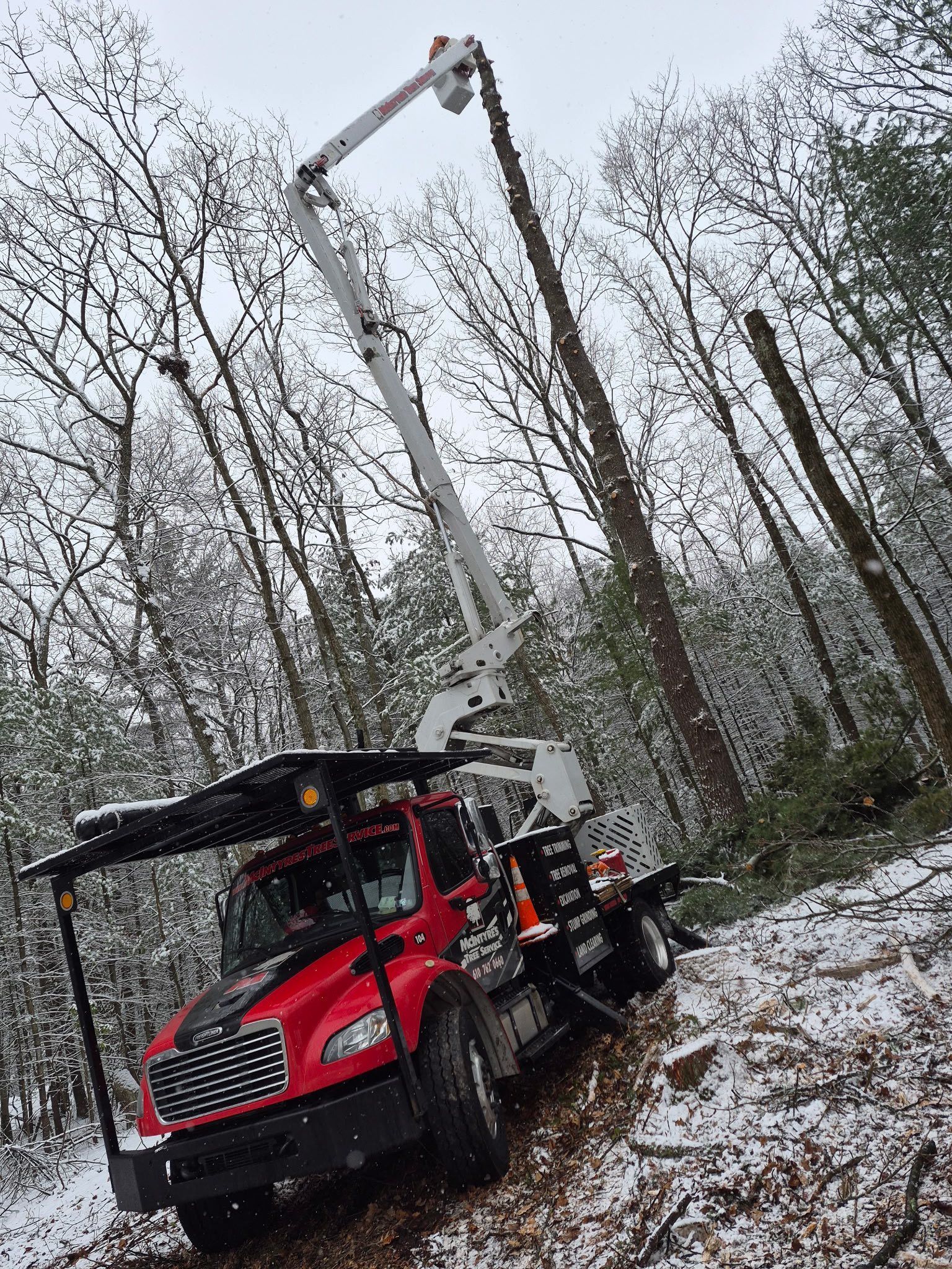 A red utility bucket truck with an extended crane arm parked in a snow-covered forest.
