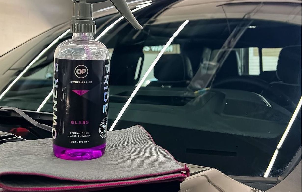 A bottle of glass cleaner is sitting on a towel next to a car.
