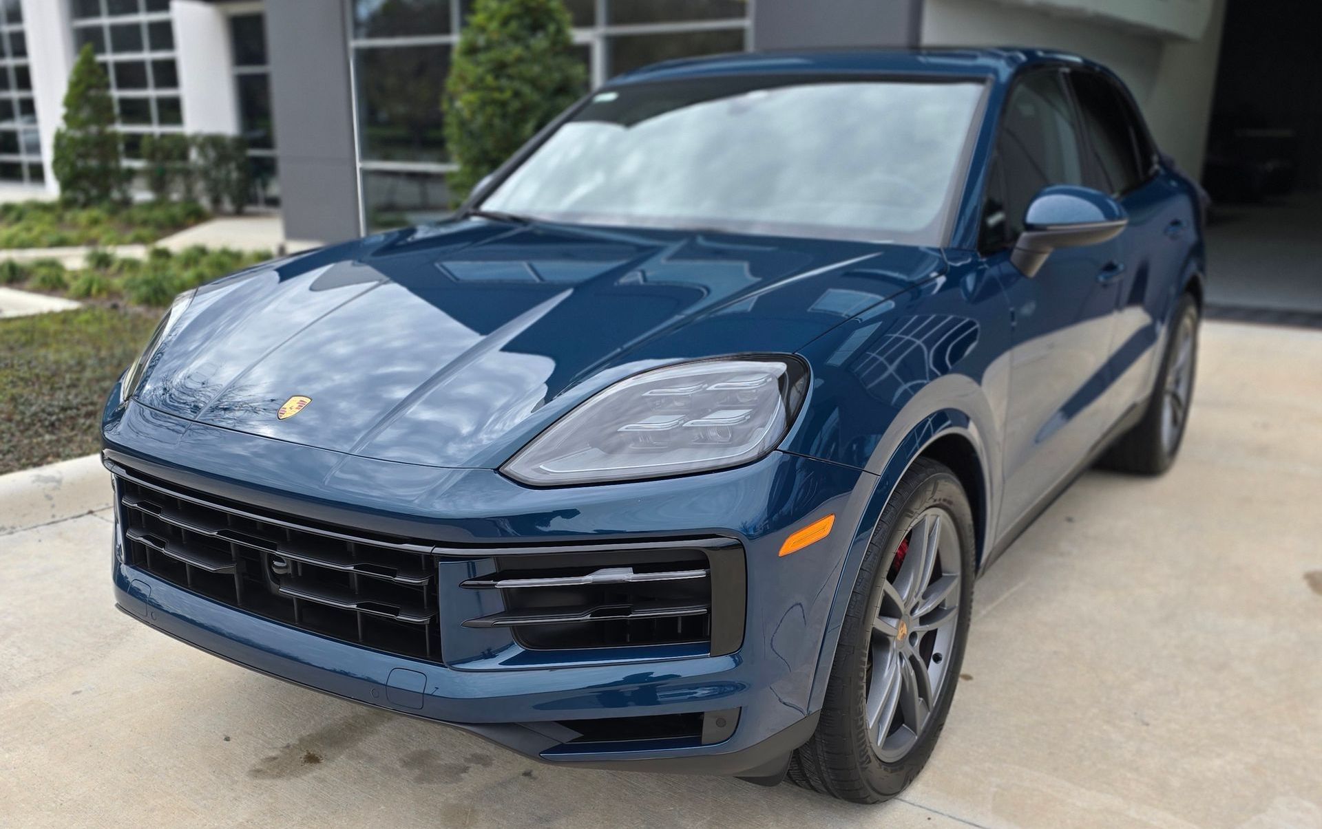 A blue porsche cayenne is parked in a parking lot in front of a building.