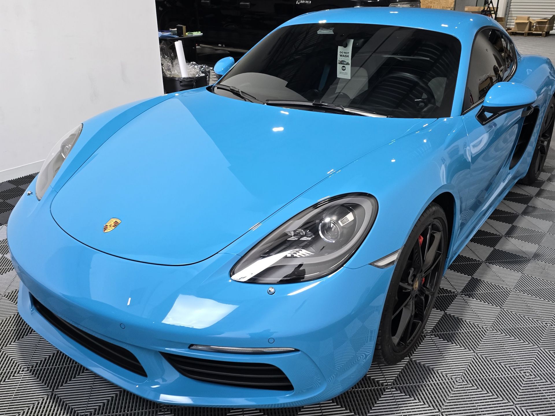 A blue porsche is parked on a checkered floor in a showroom.
