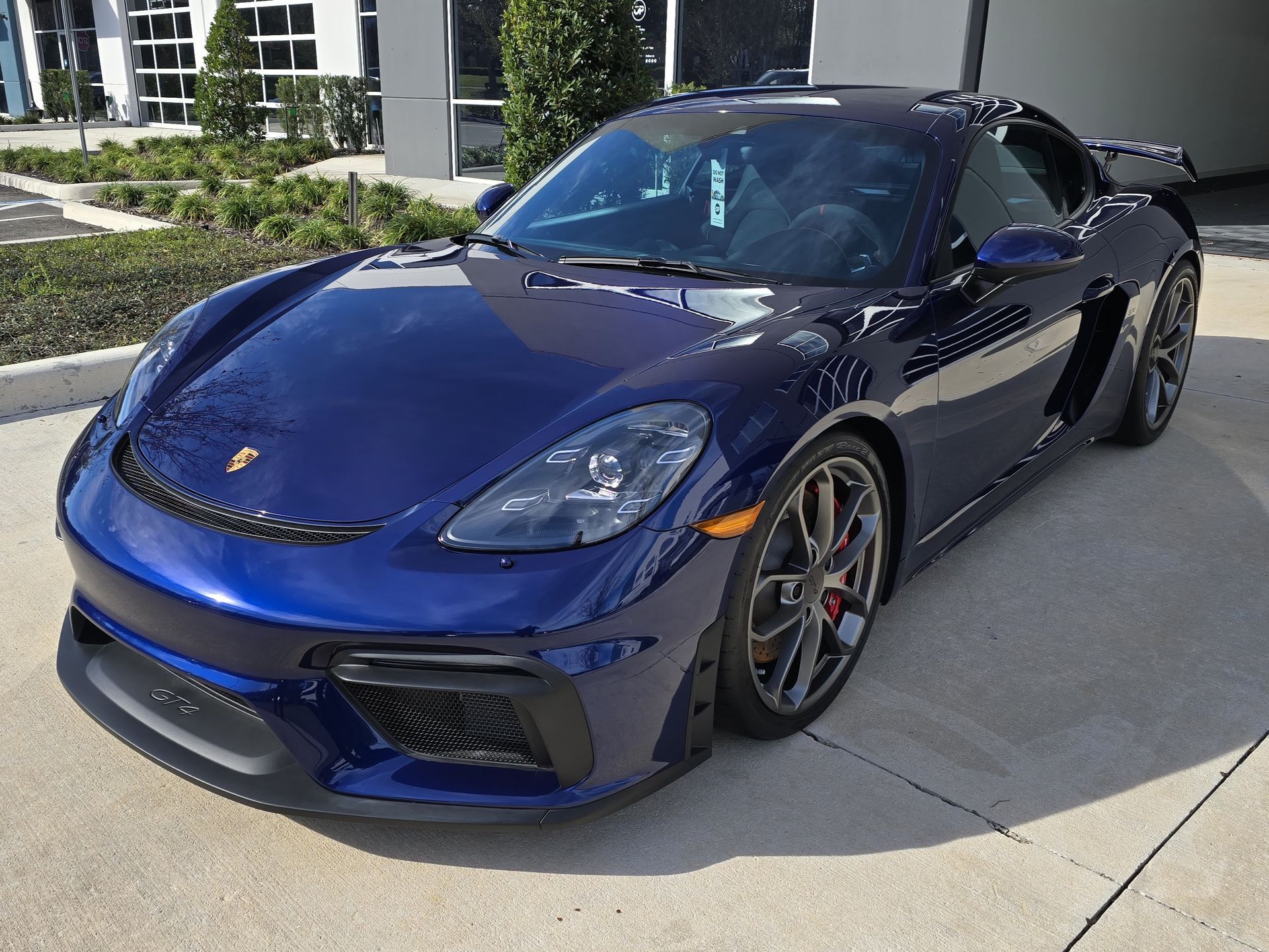 A blue sports car is parked in a parking lot in front of a building.